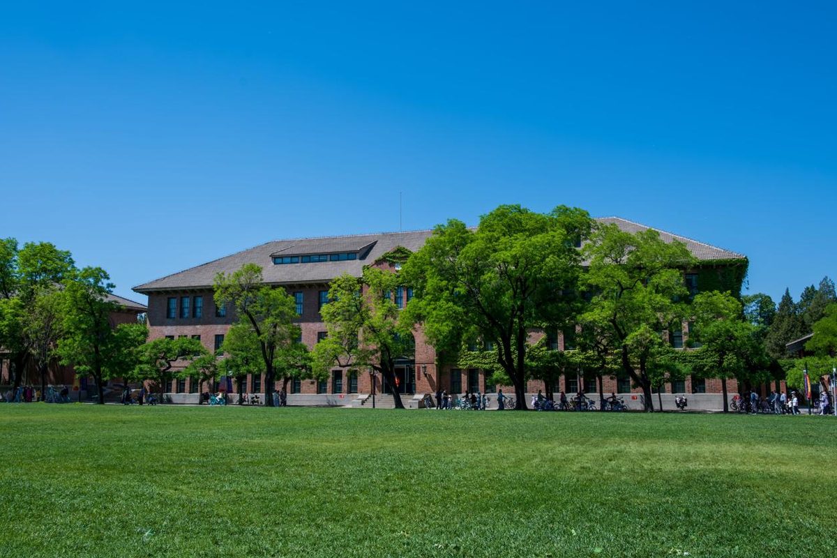 Red-brick campus building framed by trees on a sunny lawn