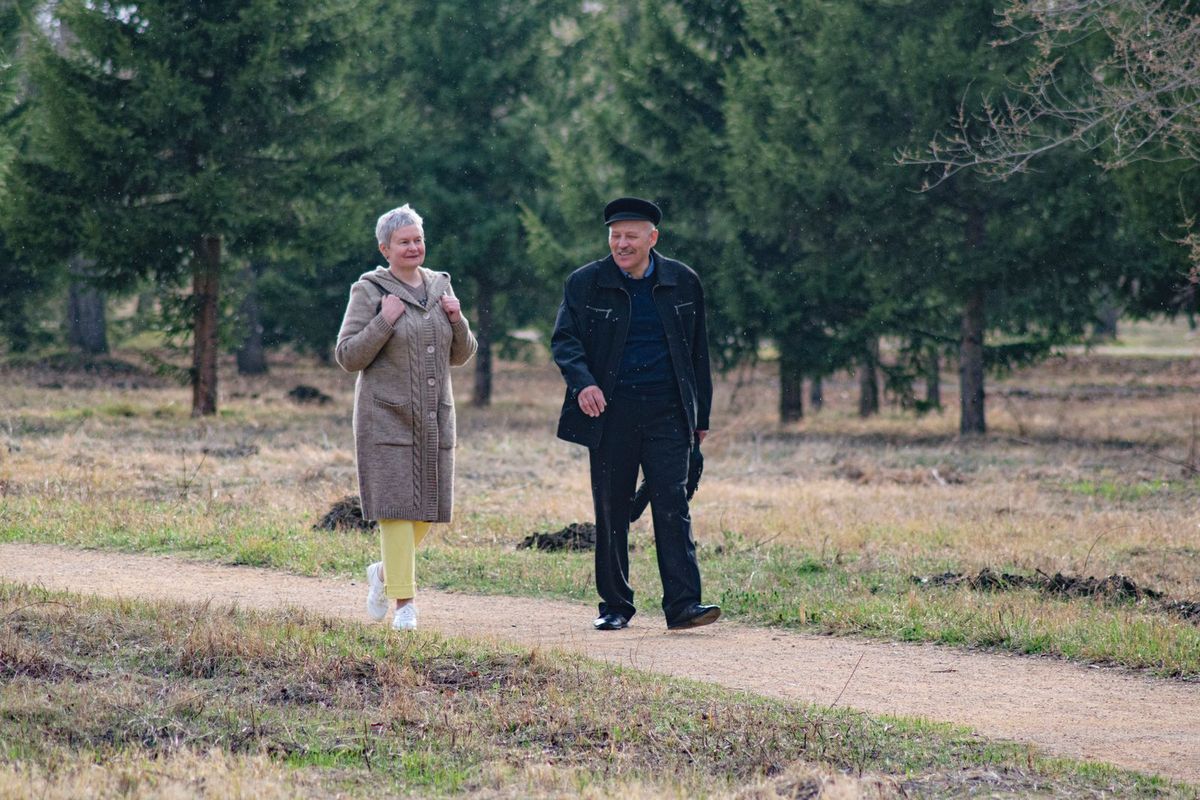 Two residents walking a gravel path through a wooded garden in soft light